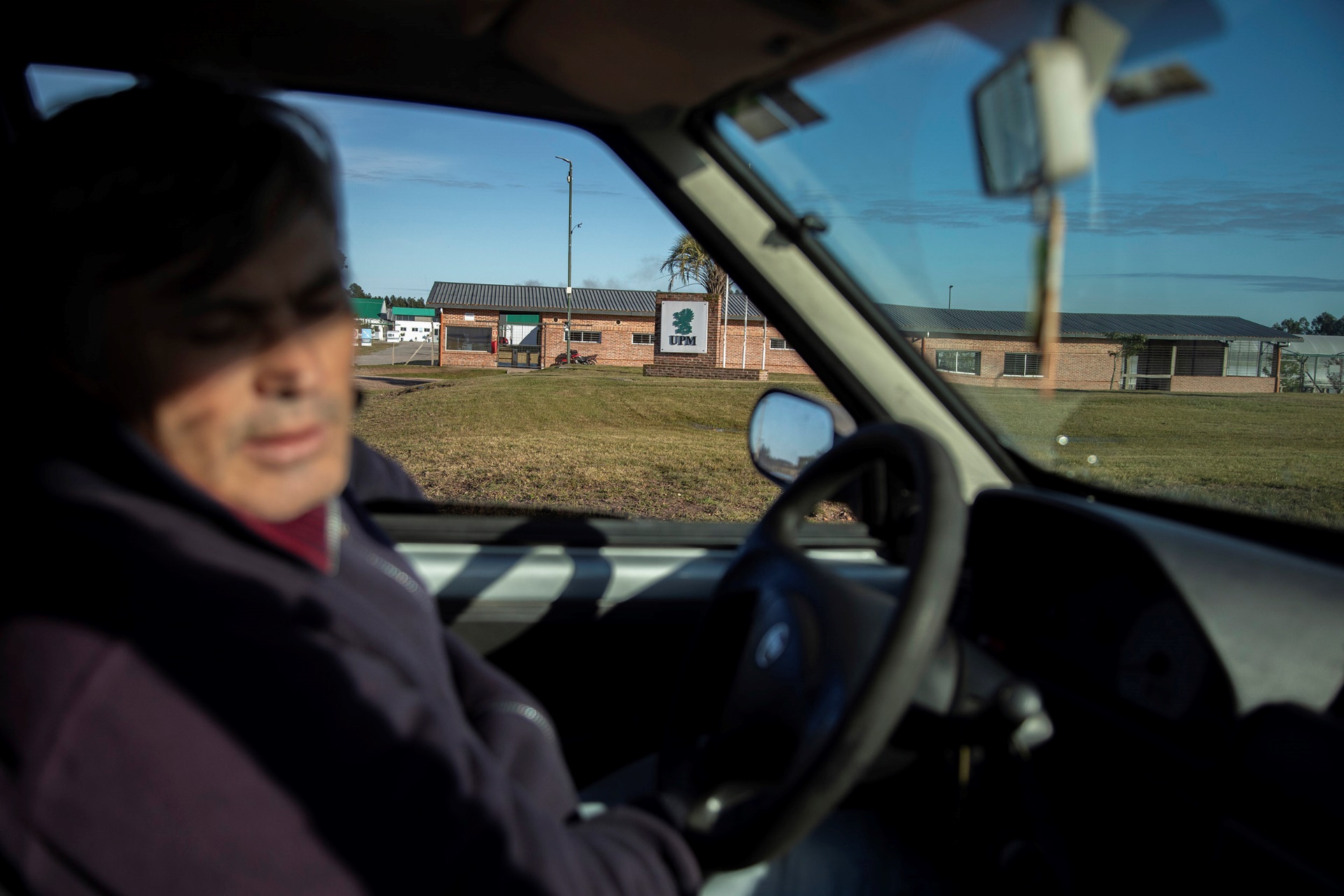 A photo of a man in the car in front of the UPM building. Marcelo Fagúndez (out of focus) in front of the main entrance of UPM's Santana Nursery.