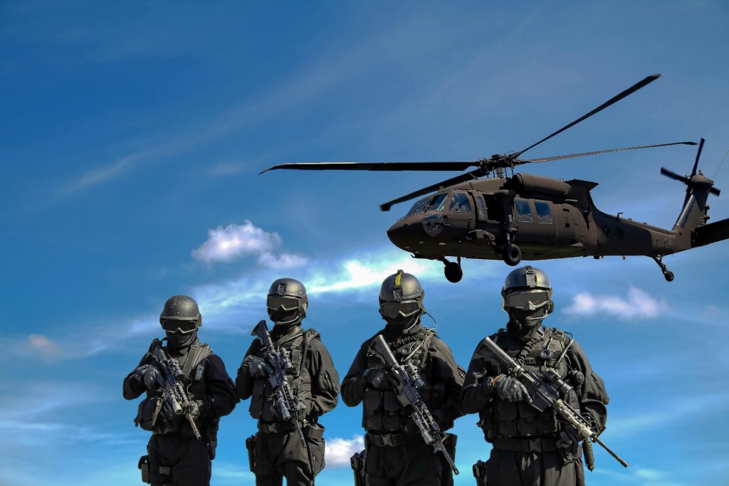 Four soldiers carrying rifles. A helicopter in the background.  
The military’s carbon footprint includes emissions from the weapons production.