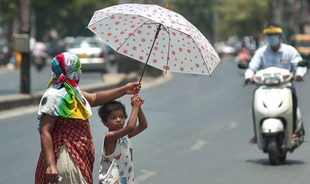 A photo of Indian woman and a child walking the street while shielding themselves from the heat with an umbrela. Symbolic image of heatwave in India.