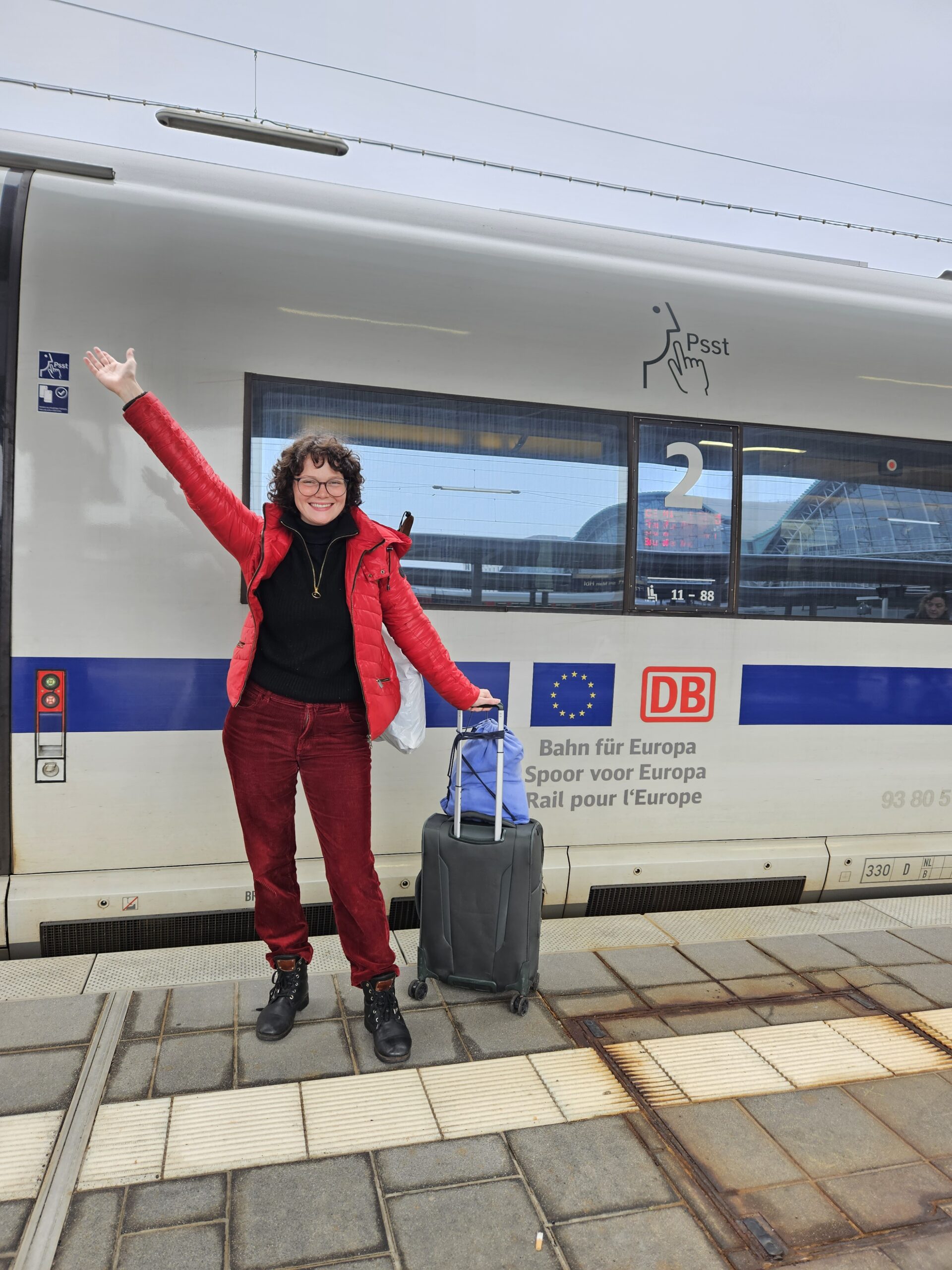 Clara Francken at a train station, with a train wagon behind her featuring the EU flag and the tagline "Rail for Europe".