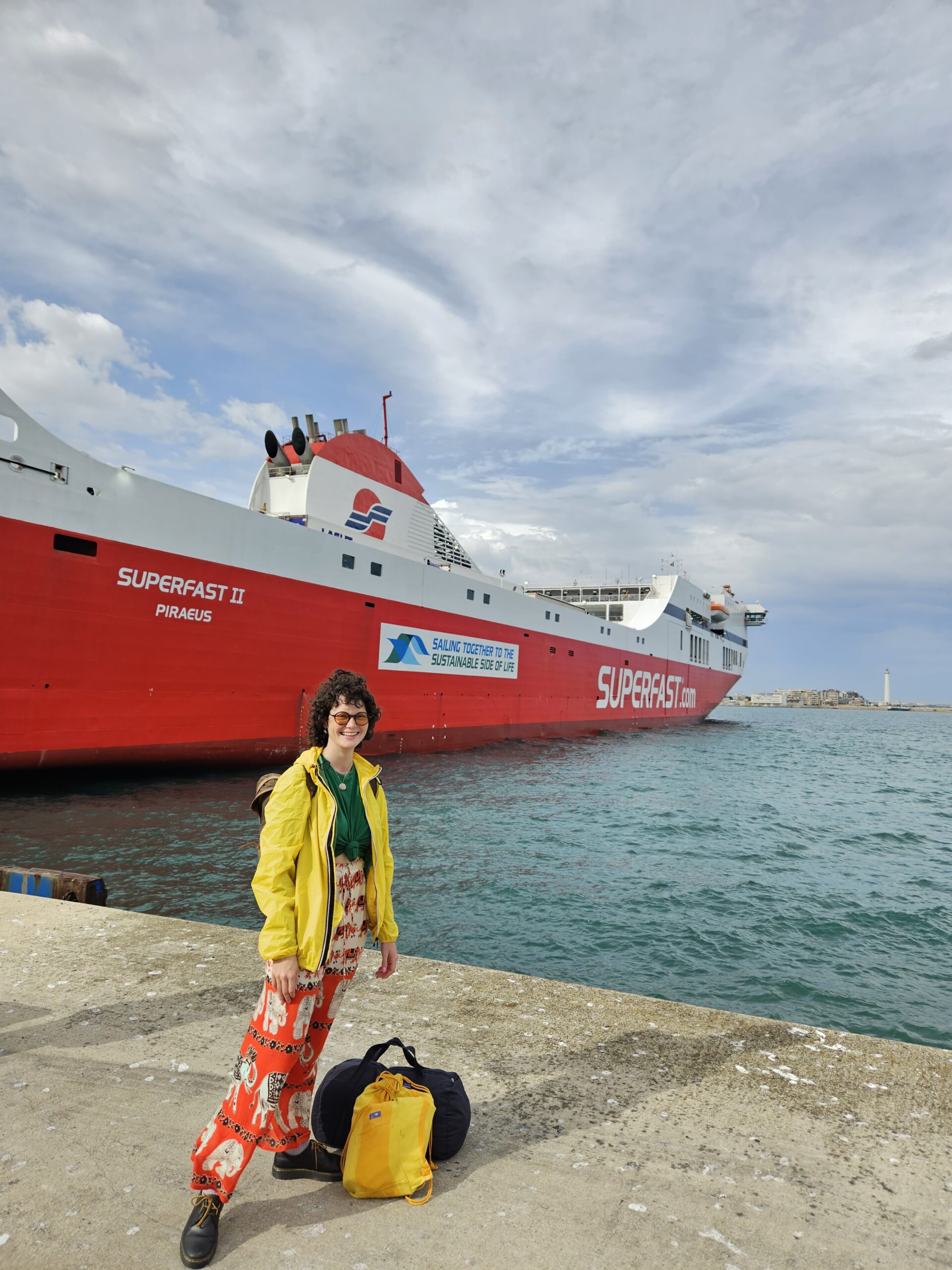 Clara Francken next to a shoreline and a boat, with her travel bags, ready to sail.