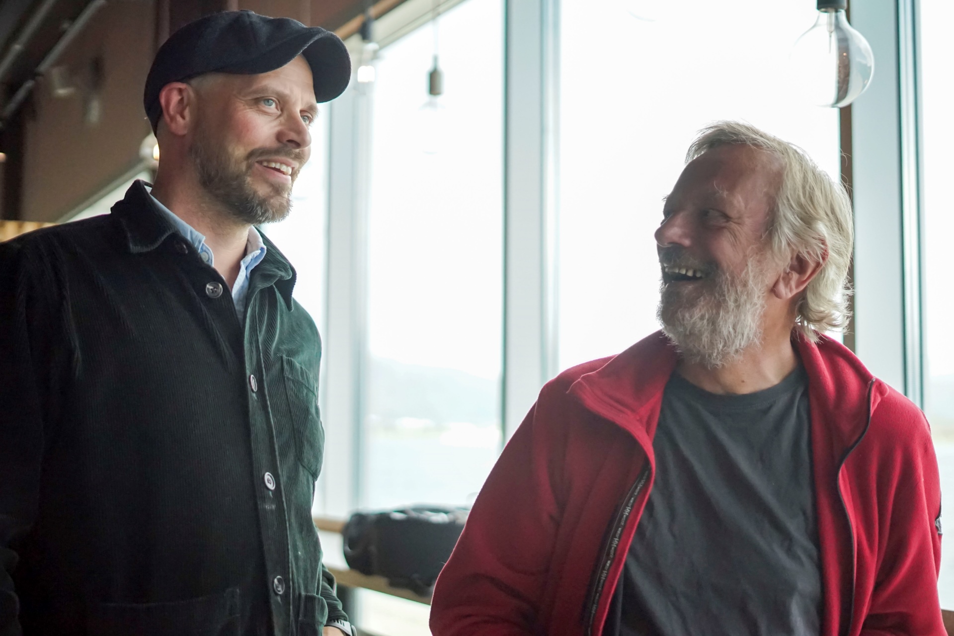 Two men smiling at each other while engaged in a conversation.