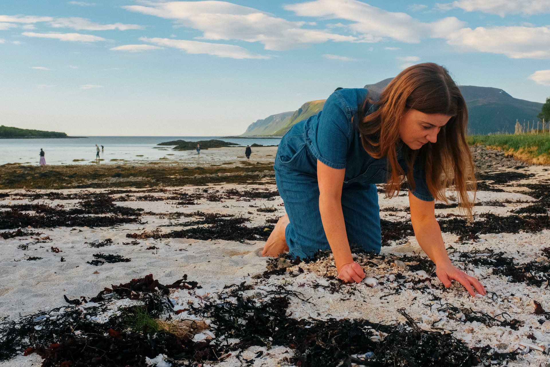 A woman (Sortland mayor Grete Ellingsen) kneeling on the beach while looking for shells in the tideline.