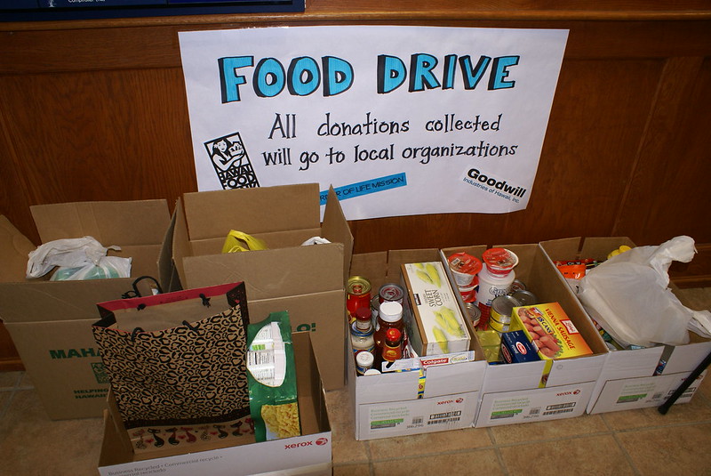 Photo of boxes filled with packaged food. The sign above reads, "Food drive: all donations collected will go to local organizations."